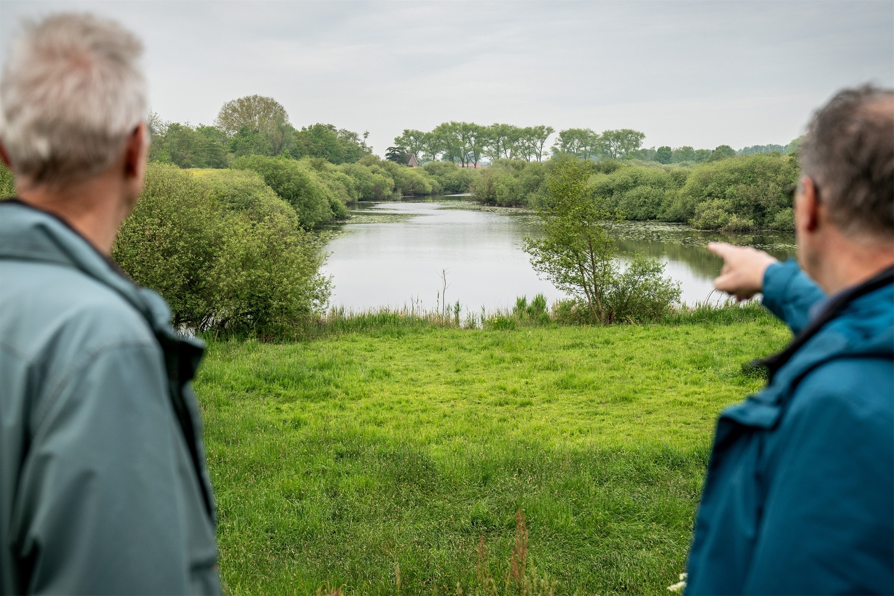 Bert Flach, links in beeld, en Tom Violier, rechts in beeld, wijzend naar een bestaande geul met beboste oevers in een verder groen gebied in het projectgebied Meanderende Maas.